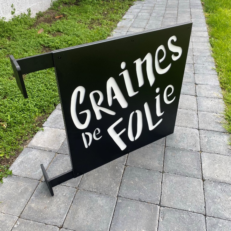 Enseigne drapeau ext&eacute;rieure Graines de Folie avec potence murale noire